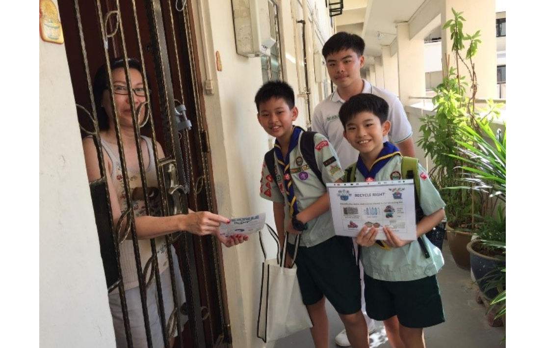 Two boy scouts with one secondary school student at a residents door, giving out pamphlet on raising Dengue Prevention awareness